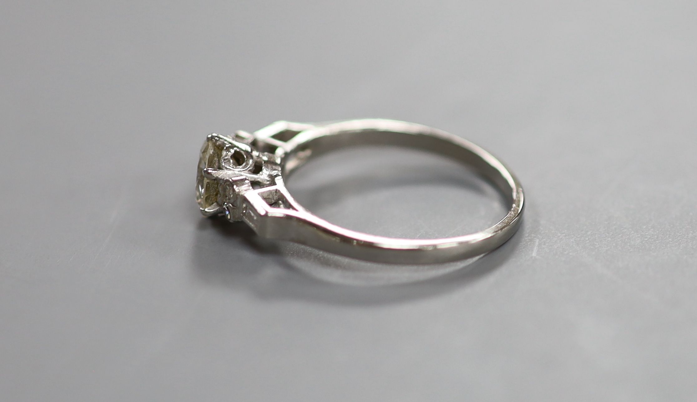 A white metal(stamped platinum) and single stone diamond ring with baguette and round cut diamond set shoulders